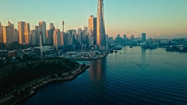 Sydney skyline at sunrise with blue skies and golden light, tilt up, aerial view.