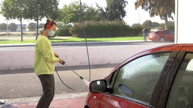 Woman cleaning hood of a red car with pressure hose and matching sweatshirt with green hair and background