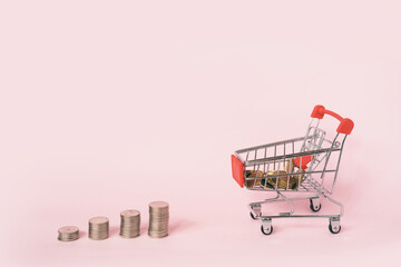 miniature shopping cart filled in coins with stack of coins on pink background for business and finance background