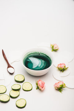 Bowl with tonic and cotton pads, cucumber slices, tea roses, and spoon with cosmetic cream on white, stock image