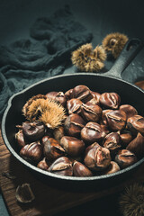 Cast iron pan with roasted chestnuts on a black background, vertical stock photo.