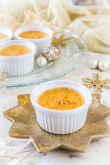 Creme brulee - traditional french vanilla cream dessert with caramelised sugar on top, served on a gold star-shaped plate with gold and white christmas decoration. Vertical stock photo.