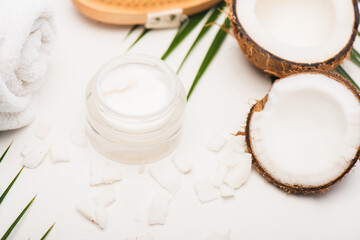 Coconut halves, flakes, container with cosmetic cream and towel on white