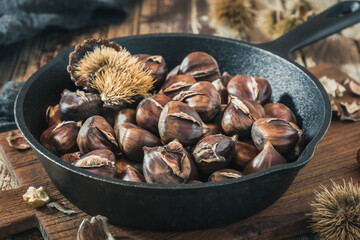 Roasted chestnuts in a cast iron pan on a wooden board