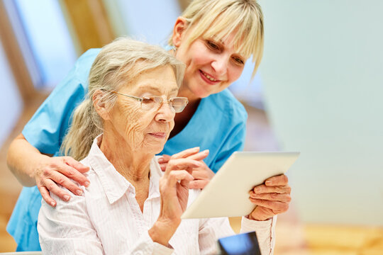 Pflegekraft hilft Seniorin mit Tablet Computer