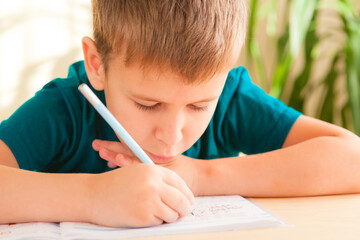 Close up of 7 years old child boy doing lessons sitting at desk in his room.