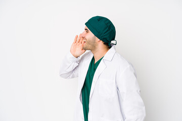 Young surgeon man isolated on white background shouting and holding palm near opened mouth.