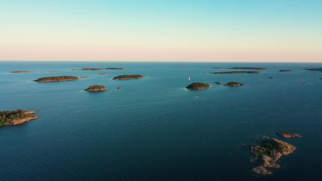 Aerial view of a sailboat, sailing between sunlit isles, warm, sunny evening, in Scandinavian archipelago - dolly, drone shot