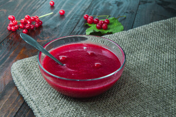 Viburnum jam in glass bowl with dessert spoon and berries on the piece of burlap. Concept of autumn breakfast