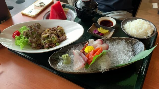 Japanese cuisine food, premium sashimi platter with rice, salad and fruits. Served on a table in restaurant.