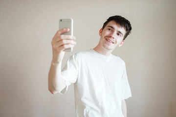 a young man makes a funny photo on his phone, smiles funny, a light teenage shield on his face,...