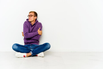 Young caucasian man sitting on the floor hugs, smiling carefree and happy.