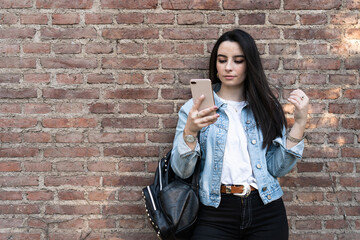 Female student with backpack looking at her phone and playing with her black hair