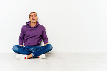 Young caucasian man sitting on the floor funny and friendly sticking out tongue.