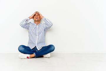 Young caucasian man sitting on the floor laughs joyfully keeping hands on head. Happiness concept.