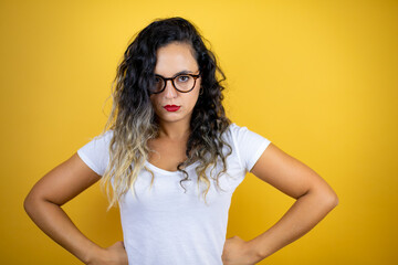 Young beautiful woman wearing casual white t-shirt over isolated yellow background skeptic and...