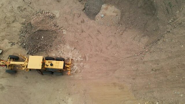 Aerial flyover of a construction grader in a dirt lot.