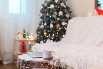 Christmas background or greeting card with laptop and coffee cup at home. Glowing snow bokeh. Winter holidays on white background. 
