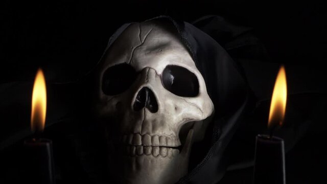 Hooded skull with two candles on dark background