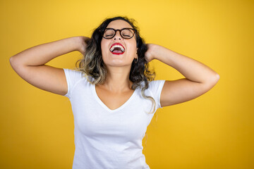 Young beautiful woman wearing casual white t-shirt over isolated yellow background relaxing and stretching, arms and hands behind head and neck smiling happy