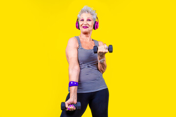 Elderly woman training using dumbbells on yellow background stretching