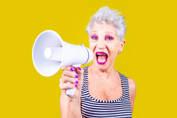 Senior woman screaming loudly in a megaphone on yellow background demonstrating