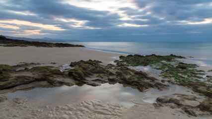 A sunrise cloudy sky reflected on a puddle on a sandy beach.