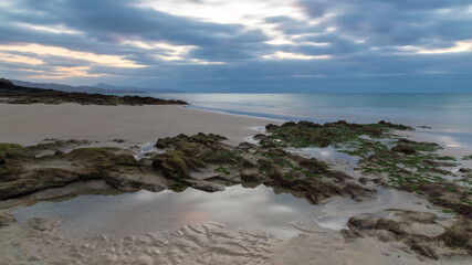Fototapeta na wymiar A sunrise cloudy sky reflected on a puddle on a sandy beach.