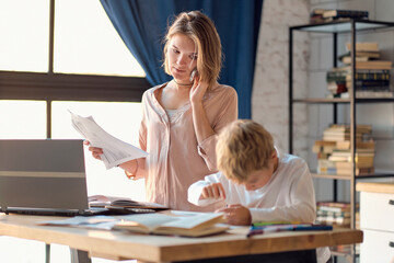 Business woman with laptop and son with tablet. multi tasking, freelance and motherhood concept working at home as her cute little boy plays on a tablet alongside her as she works