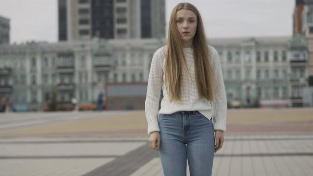 Stressed young Caucasian woman standing on urban city square and looking around. Panic attack of beautiful slim lady outdoors in town. Stressful lifestyle concept.