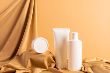 Group of cosmetics tubes bottles abstract podium yellow background draped cloth.