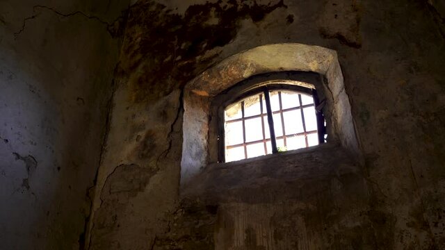 Window of dungeon with irons and ruined dirty walls inside medieval fortress, historic place