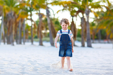 Adorable active little kid boy having fun on tropical beach of island. Happy cute child relaxing, playing, enjoying, running and jumping on sunny warm day near palms and ocean. Active family vacations