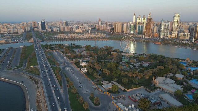 Drone view of Sharjah's Khalid Lake and city skyline on a beautiful evening, Eye of Emirates Wheel, Travel tourism business in the United Arab Emirates. 4k Footage