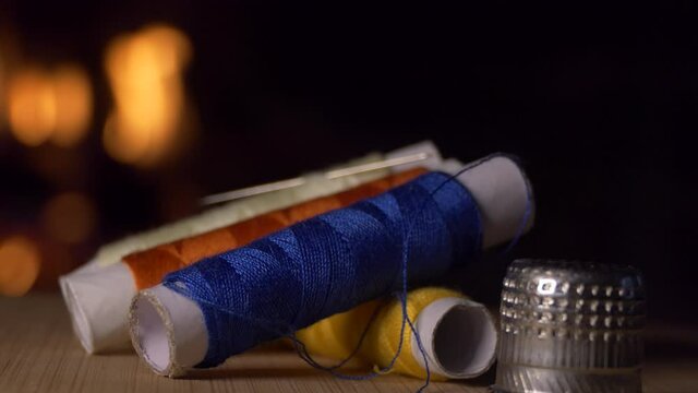 Coils of colored thread and a thimble rotate against the background of the fireplace flame. Close-up shooting.