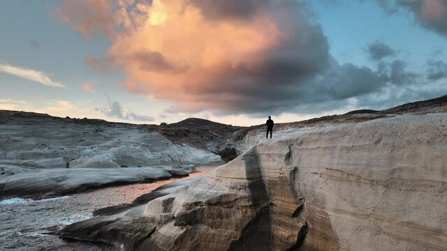 Aerial jib up shot of a man standing at the edge of a cliff on Sarakiniko beach at sunset