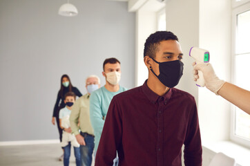 Obraz premium Man, standing in line in public place, gets his body temperature measured with infrared thermometer