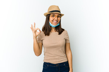 Young latin woman wearing hat and mask to protect from covid isolated on white background cheerful and confident showing ok gesture.