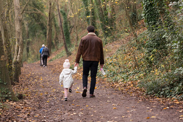 A man holding his daughters hand walking through a forest in autumn