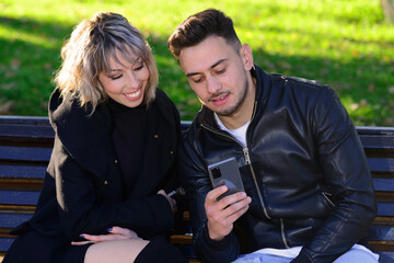 Two young friends sitting on a park bench talking consulting the mobile