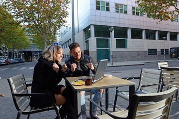 Two young friends having a drink on the terrace of a bar and using a laptop