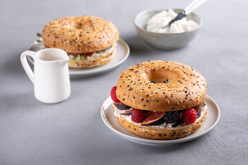 Bagel with cream cheese, figs, raspberries, blackberries and honey.  Gourmet sandwich on gray background.
