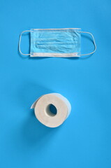 Obraz premium Blue Face protective masks and a roll of toilet paper on a blue background. Copy space, covid - 19