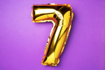 Creative layout. Golden foil balloon number and digit seven 7. Birthday greeting card. Anniversary concept. Top view. Copy space. Stylish gold numeral over purple background. Numerical digit.