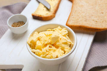 Bowl with fresh butter and bread on wooden board