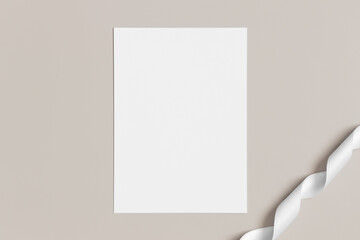 White invitation card mockup with a satin tape on a beige background. 5x7 ratio, similar to A6, A5.