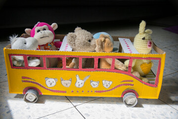 Homemade bus for kids, made of cardboard, painted yellow, with dolls as passengers. 