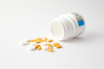 A closeup of white and yellow pills drop out of the pill bottle on the white surface © Carlos