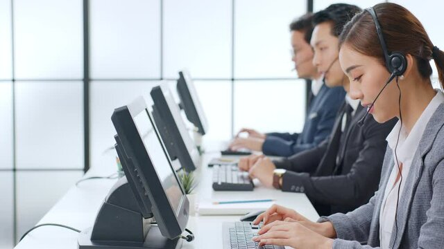 Asian call center team, customer service, telesales in formal suit wearing headset or headphone talking with customer in modern office