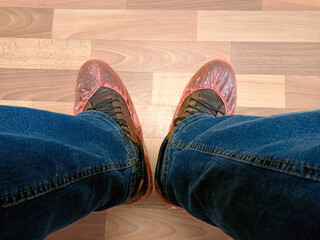 Disposable orange shoe covers on the feet in brown shoes and blue jeans.
